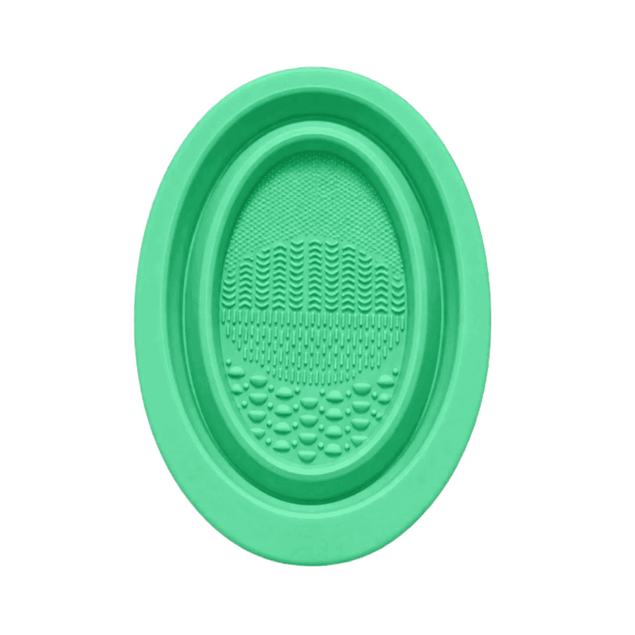 Green oval silicone facial cleansing brush with textured surface and raised cleansing bristles.
